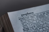 A close-up image of a dictionary page, focusing on the word 'prophecy' along with its pronunciation guide and definitions. The text includes etymological information, indicating its origins from Latin and Greek.