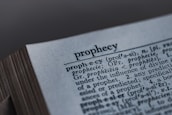 A close-up image of a dictionary page, focusing on the word 'prophecy' along with its pronunciation guide and definitions. The text includes etymological information, indicating its origins from Latin and Greek.
