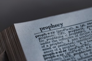 A close-up image of a dictionary page, focusing on the word 'prophecy' along with its pronunciation guide and definitions. The text includes etymological information, indicating its origins from Latin and Greek.
