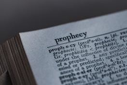 A close-up image of a dictionary page, focusing on the word 'prophecy' along with its pronunciation guide and definitions. The text includes etymological information, indicating its origins from Latin and Greek.