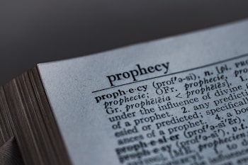 A close-up image of a dictionary page, focusing on the word 'prophecy' along with its pronunciation guide and definitions. The text includes etymological information, indicating its origins from Latin and Greek.