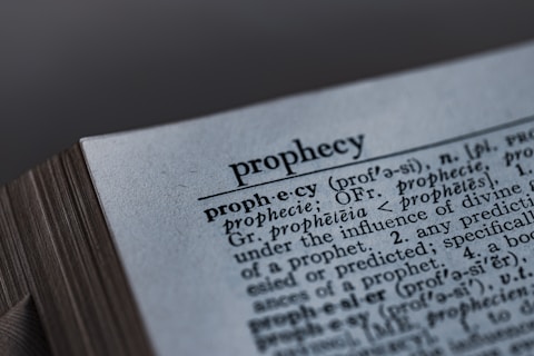 A close-up image of a dictionary page, focusing on the word 'prophecy' along with its pronunciation guide and definitions. The text includes etymological information, indicating its origins from Latin and Greek.