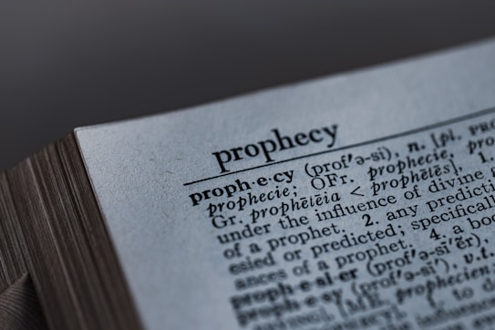 A close-up image of a dictionary page, focusing on the word 'prophecy' along with its pronunciation guide and definitions. The text includes etymological information, indicating its origins from Latin and Greek.