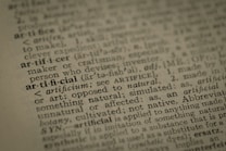 A close-up view of a dictionary page highlighting the word 'artificial' along with its pronunciation, part of speech, and definition. The text surrounding 'artificial' is printed in a traditional serif font on a slightly textured paper.
