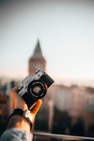 Close-up of a traveler’s hand holding a vintage camera against a backdrop of winding city streets.