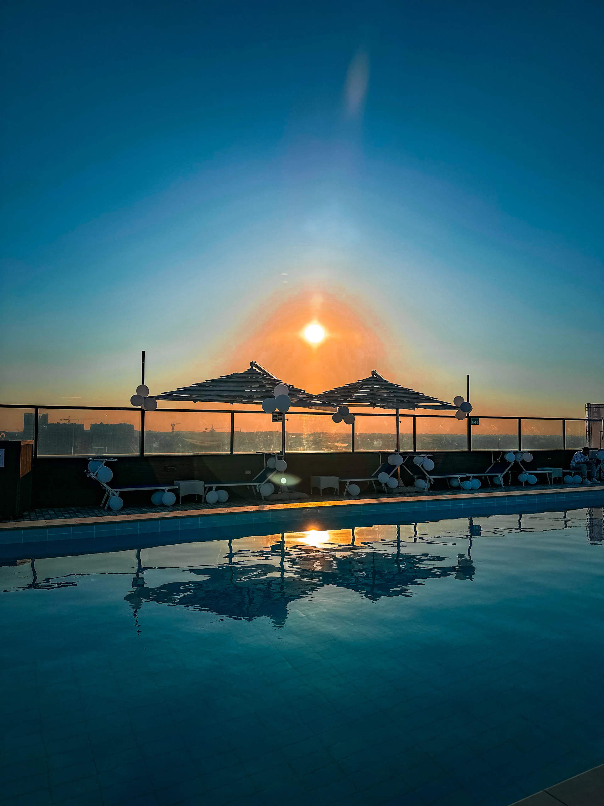 A serene rooftop pool area overlooking the Dubai Marina, bathed in warm evening light.