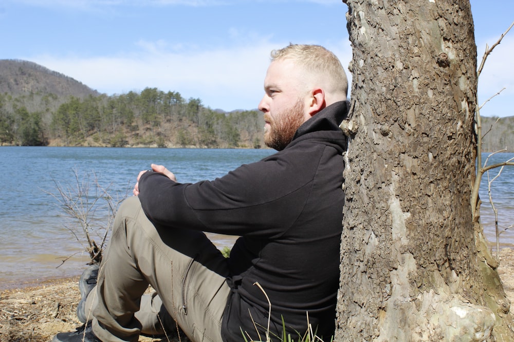 a man sitting next to a tree near a body of water