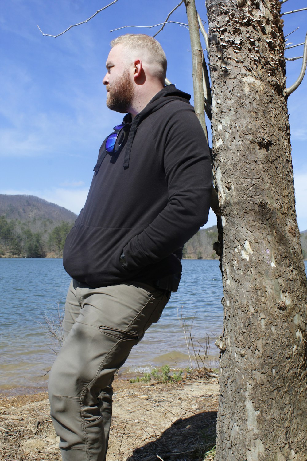 a man leaning against a tree next to a body of water