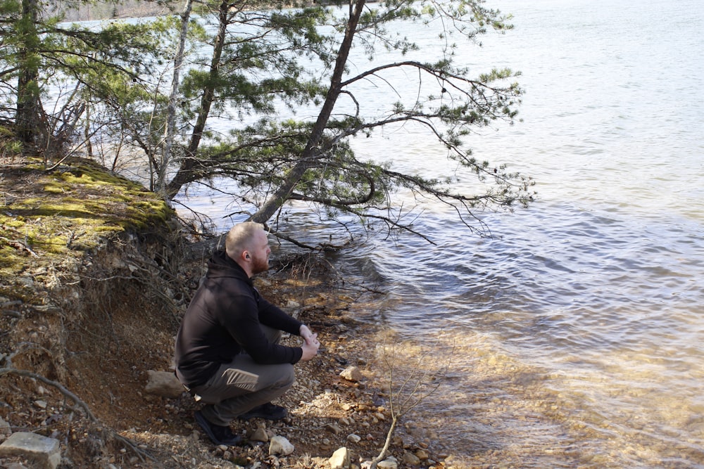 a man sitting on a rock next to a body of water