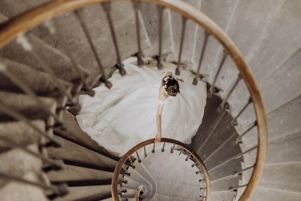 a woman in a wedding dress walking down a spiral staircase