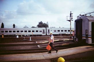 A railway worker using a tablet on site beside train tracks under a clear blue sky.