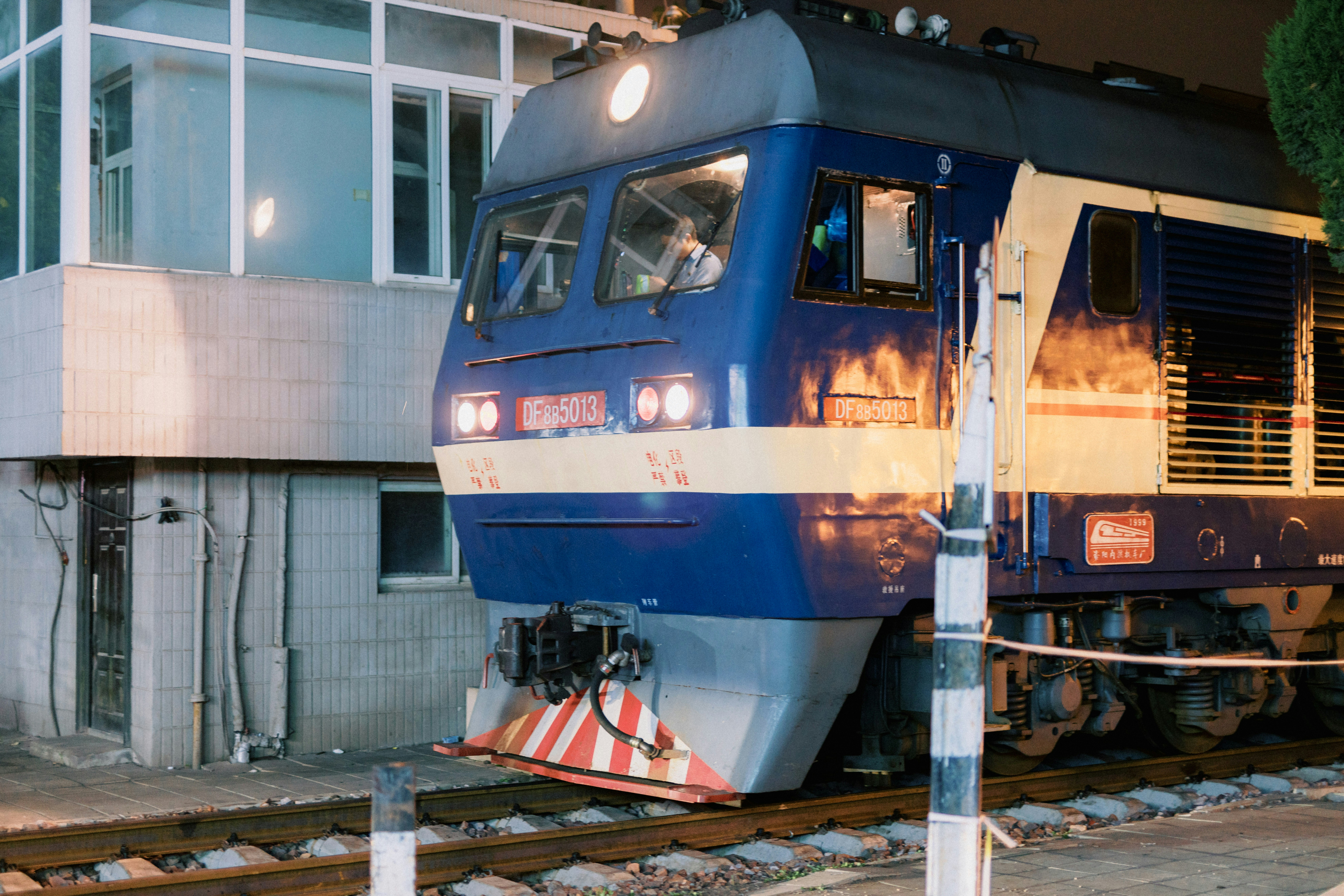 a blue train traveling past a tall white building