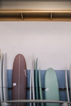 A row of colorful finished surfboards leaning against a wooden wall.