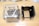 Two plastic containers are placed side by side on a wooden floor. The one on the left is transparent with clear sides showing its internal structure, and the one on the right has black, vertical slats and a more solid appearance. Both have handles on their sides.