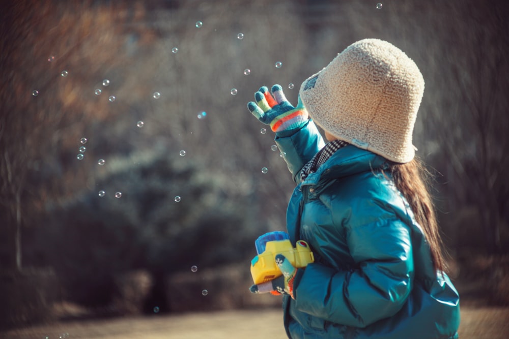 a little girl in a blue jacket blowing bubbles