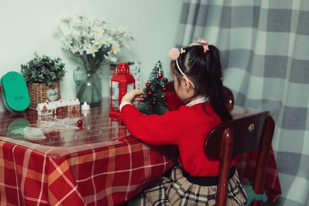 a little girl sitting at a table with a christmas tree