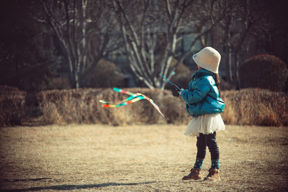 a little girl standing in a field flying a kite