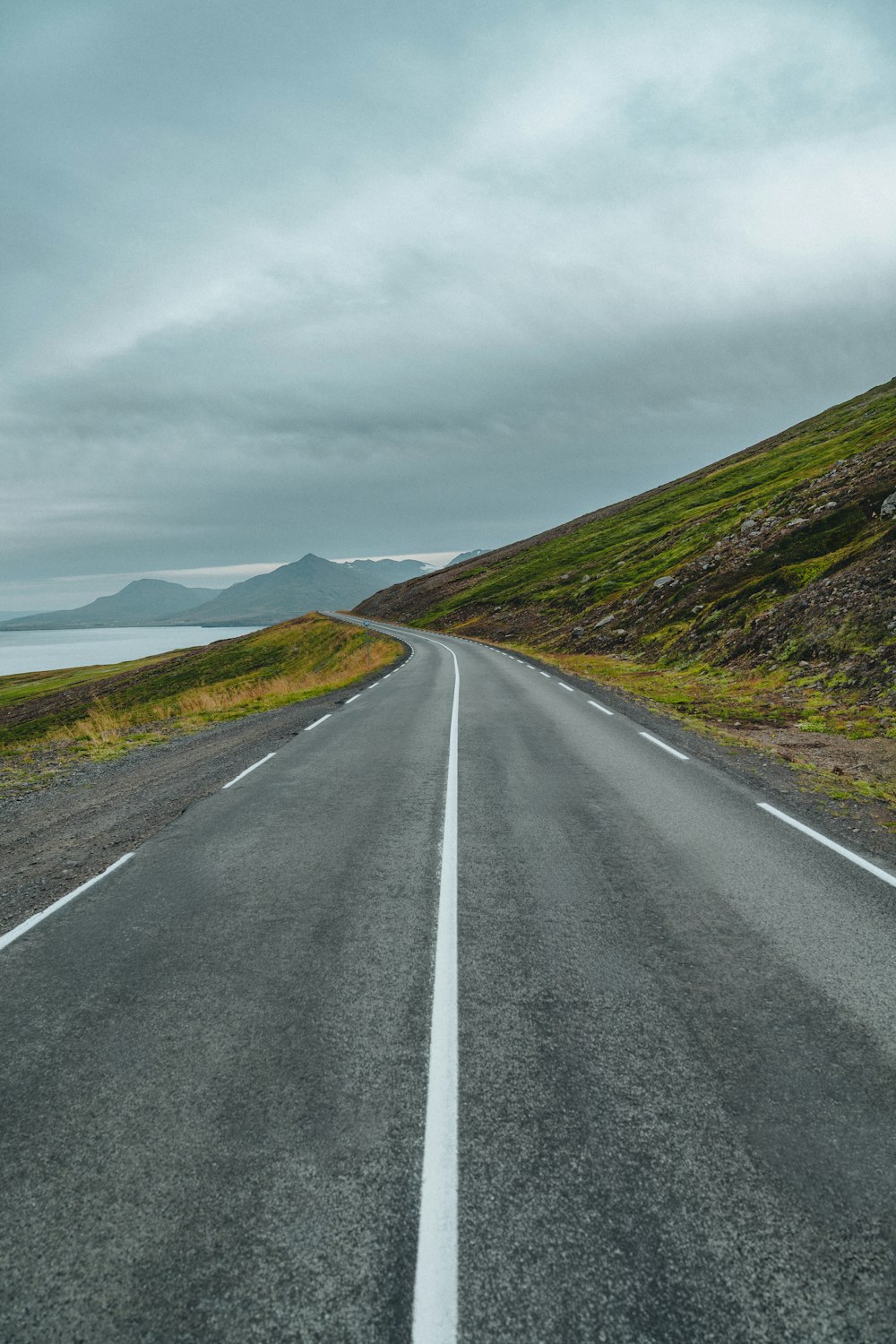 an empty road on a cloudy day with mountains in the background
