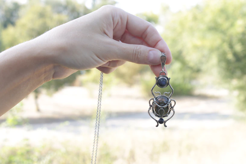 A serene close-up of a hand holding a delicate Kabbalah tree of life pendant glowing softly in blue and violet hues.