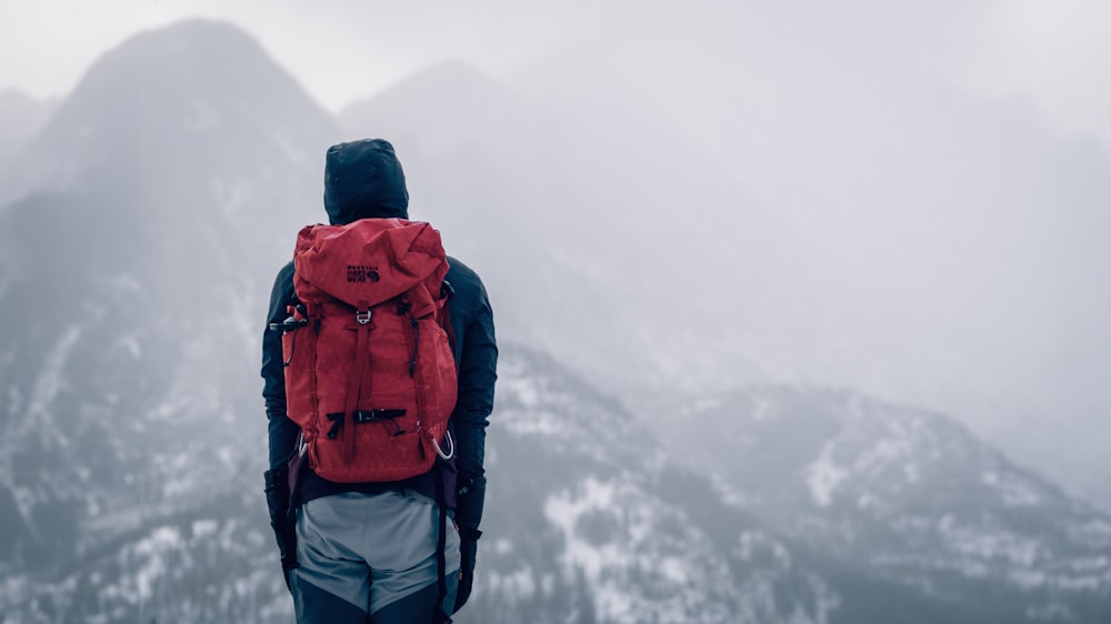 a man with a red backpack standing on top of a mountain