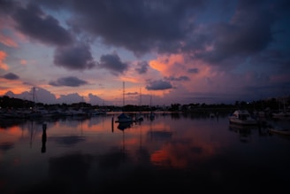A serene marina at sunset with boats docked and calm waters reflecting the colorful sky.