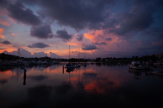 A serene marina at sunset with boats docked and calm waters reflecting the colorful sky.