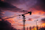 Sunset silhouette of a crane towering over a cityscape, signaling progress and growth.