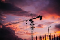 Sunset silhouette of a crane towering over a developing urban area in Saudi Arabia.