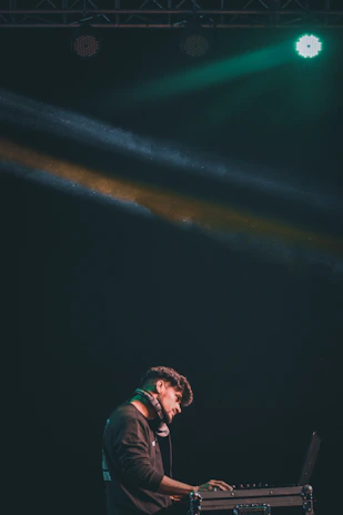A DJ mixing live on stage with a focused expression, illuminated by neon light beams.