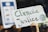 A cardboard sign with the words 'Climate Justice' written in green and black is being held up. The sign also features an illustration of the Earth. A date, '15.09.2023,' is visible on the top right corner of the sign. The background is blurred, with hints of other signs or people, suggesting a rally or protest.