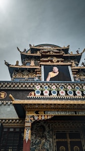 An ornate and traditional building showcasing intricate details and vibrant decorations, featuring colorful patterns and a large portrait of a person in ceremonial attire. The architecture is adorned with gold accents and symbolic illustrations.