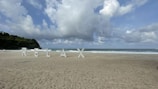 Large letters spelling out 'RELAX' are positioned on a sandy beach with waves in the background. The sky is partly cloudy, and there is lush greenery on the left side.