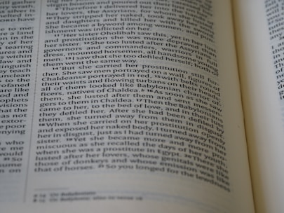 The image features a close-up view of an open book with text in English. The focus is on two main pages with text in a clear, serif font, showing paragraphs and numbered verses.