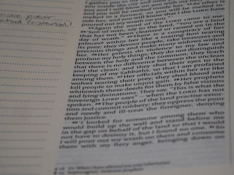 A close-up view of an open book with text on one page and a lined margin on the left side for notes. The text includes references to religious or biblical content, with some words highlighted or bolded. Handwritten notes are visible in the margin.