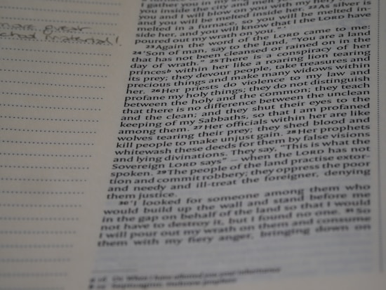A close-up view of an open book with text on one page and a lined margin on the left side for notes. The text includes references to religious or biblical content, with some words highlighted or bolded. Handwritten notes are visible in the margin.