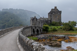 Old Scottish castle entrance with heavy iron gates overlooking misty water.