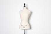 A beige dress form or mannequin torso is placed in front of a plain white background. The top of the mannequin has a black neck and features the inscription 'HAUTE COUTURE STOCKMAN PARIS'. The focus is on the elegant shape and neutral tone of the form.