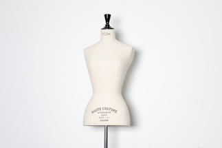 A beige dress form or mannequin torso is placed in front of a plain white background. The top of the mannequin has a black neck and features the inscription 'HAUTE COUTURE STOCKMAN PARIS'. The focus is on the elegant shape and neutral tone of the form.