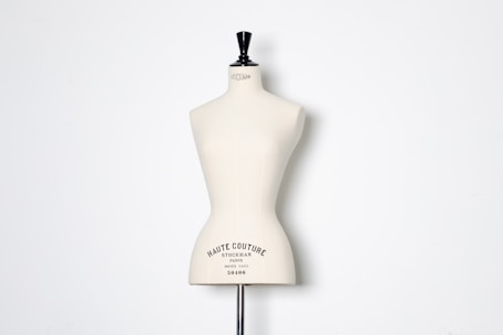 A beige dress form or mannequin torso is placed in front of a plain white background. The top of the mannequin has a black neck and features the inscription 'HAUTE COUTURE STOCKMAN PARIS'. The focus is on the elegant shape and neutral tone of the form.