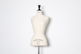 A beige dress form or mannequin torso is placed in front of a plain white background. The top of the mannequin has a black neck and features the inscription 'HAUTE COUTURE STOCKMAN PARIS'. The focus is on the elegant shape and neutral tone of the form.