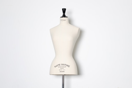 A beige dress form or mannequin torso is placed in front of a plain white background. The top of the mannequin has a black neck and features the inscription 'HAUTE COUTURE STOCKMAN PARIS'. The focus is on the elegant shape and neutral tone of the form.