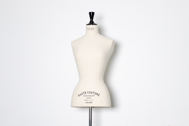 A beige dress form or mannequin torso is placed in front of a plain white background. The top of the mannequin has a black neck and features the inscription 'HAUTE COUTURE STOCKMAN PARIS'. The focus is on the elegant shape and neutral tone of the form.