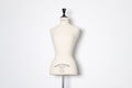 A beige dress form or mannequin torso is placed in front of a plain white background. The top of the mannequin has a black neck and features the inscription 'HAUTE COUTURE STOCKMAN PARIS'. The focus is on the elegant shape and neutral tone of the form.