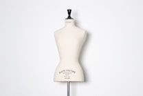 A beige dress form or mannequin torso is placed in front of a plain white background. The top of the mannequin has a black neck and features the inscription 'HAUTE COUTURE STOCKMAN PARIS'. The focus is on the elegant shape and neutral tone of the form.