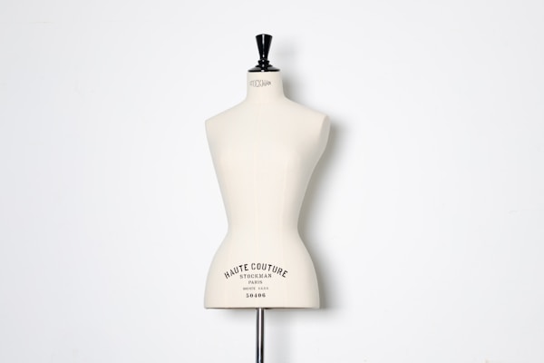 A beige dress form or mannequin torso is placed in front of a plain white background. The top of the mannequin has a black neck and features the inscription 'HAUTE COUTURE STOCKMAN PARIS'. The focus is on the elegant shape and neutral tone of the form.