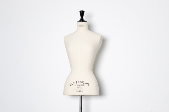 A beige dress form or mannequin torso is placed in front of a plain white background. The top of the mannequin has a black neck and features the inscription 'HAUTE COUTURE STOCKMAN PARIS'. The focus is on the elegant shape and neutral tone of the form.