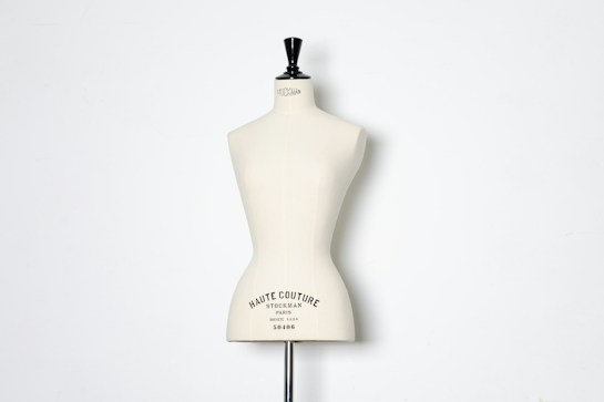 A beige dress form or mannequin torso is placed in front of a plain white background. The top of the mannequin has a black neck and features the inscription 'HAUTE COUTURE STOCKMAN PARIS'. The focus is on the elegant shape and neutral tone of the form.