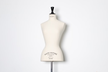 A beige dress form or mannequin torso is placed in front of a plain white background. The top of the mannequin has a black neck and features the inscription 'HAUTE COUTURE STOCKMAN PARIS'. The focus is on the elegant shape and neutral tone of the form.