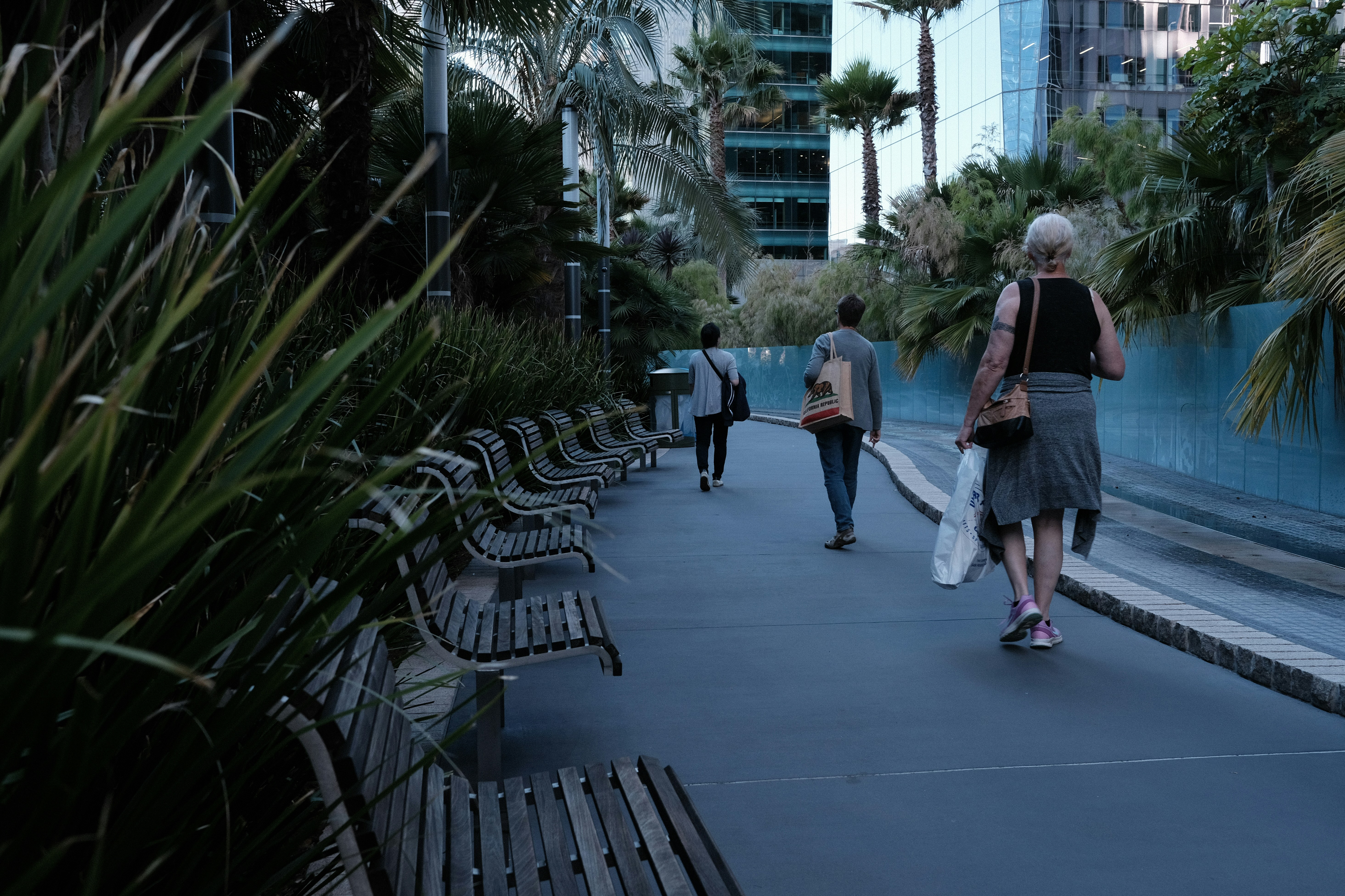 a group of people walking down a sidewalk next to benches