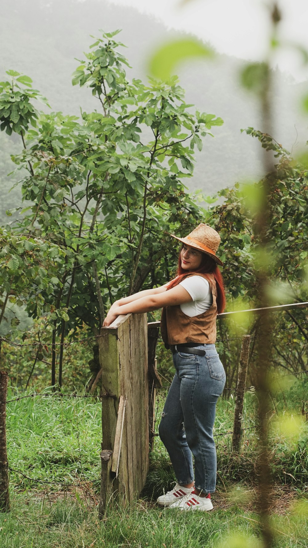 a woman leaning on a wooden post in a field